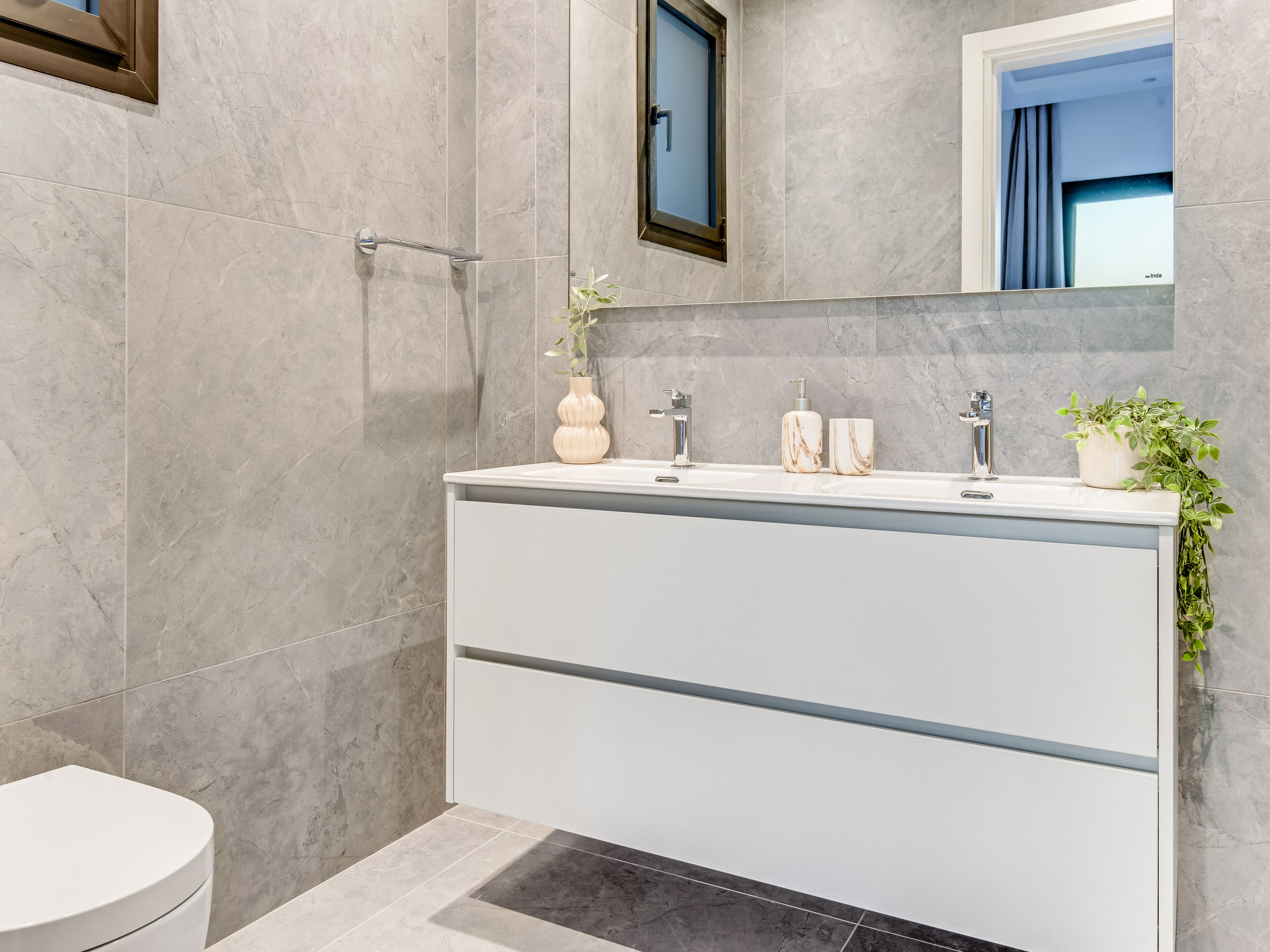 A modern bathroom with a white vanity, marble tiles, a shower area, and a potted plant.
