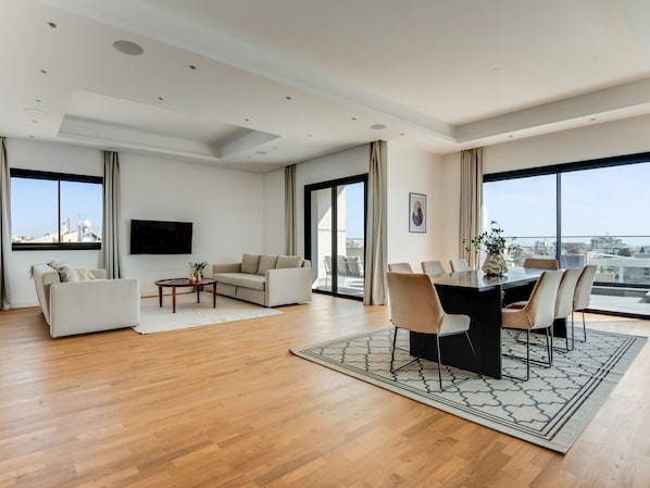 A spacious living room with a sofa, coffee table, and dining area with chairs and a table. - Sanders Crystal 1 - Large 4-bdr Penthouse With Shared Pool (Limassol)