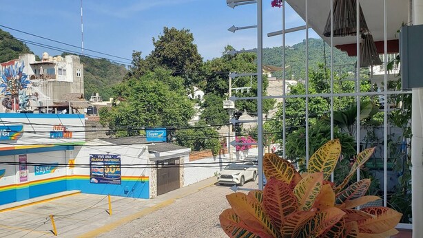 A view from a balcony overlooking a street with a Sayer bank branch, a parked car, and a mountain in the background.