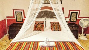 Un lit à baldaquin, deux tables de chevet, un ventilateur fixé au mur et des tapis à motifs.