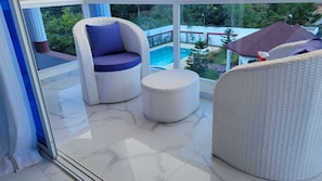 Ein Balkon mit Korbmöbeln, ein Pool und Blick ins umliegende Grün.