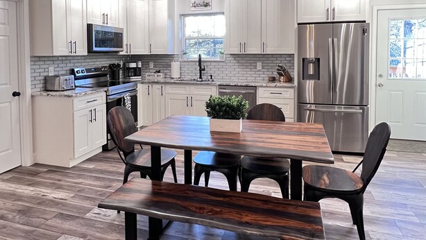 A modern kitchen with white cabinets, stainless steel appliances, and a wooden dining table. - Mountain View Modern Cottage in the Smokies W/ Hot Tub, Newly Renovated. (Sevierville)