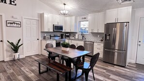 A modern kitchen with white cabinets, a stainless steel refrigerator, a dining table with chairs, and a bench. - Mountain View Modern Cottage in the Smokies W/ Hot Tub, Newly Renovated. (Sevierville)