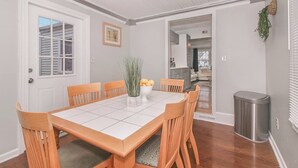 A dining room with a white tiled table, wooden chairs, a vase with flowers, and a trash can. - NICE New Kitchen, King Bed, Fenced Yard, 2 baths, Close to Airport & Downtown (Cleveland)