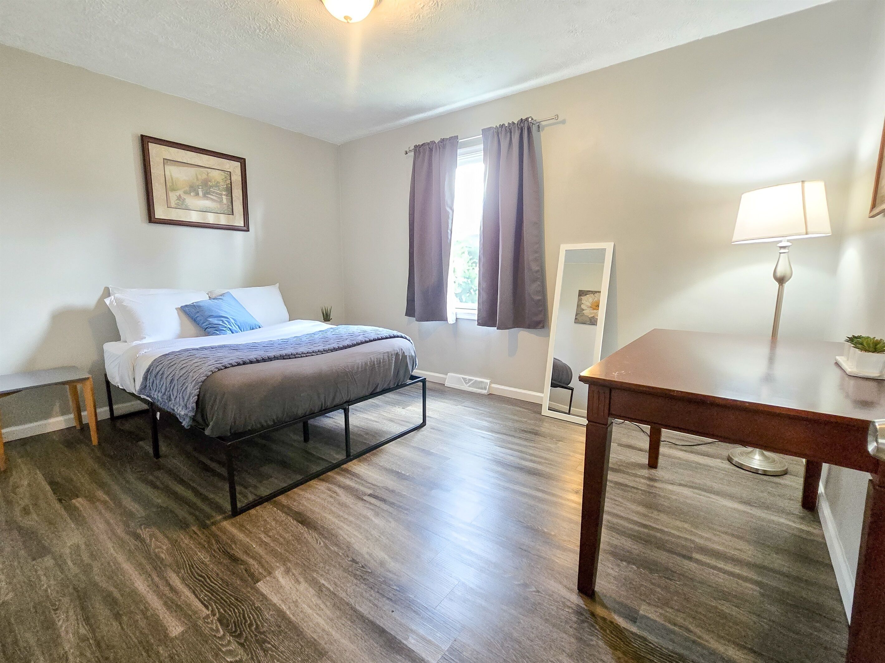 A bedroom with a bed, bedside table, lamp, and a mirror.