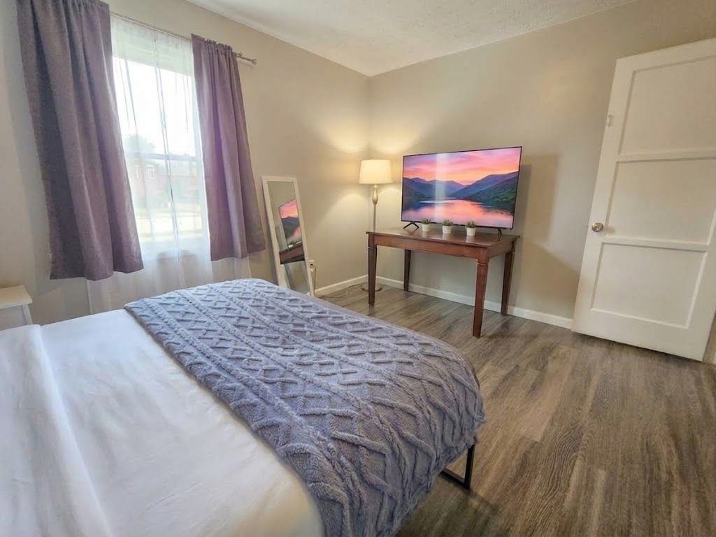 Ein Hotelzimmer mit einem Bett, einem Fernseher auf einem Schrank, einer Tür und einem Fenster mit Vorhängen.