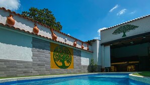 Una piscina con solárium de baldosas, un mural de un árbol y un edificio con logotipo de árbol.