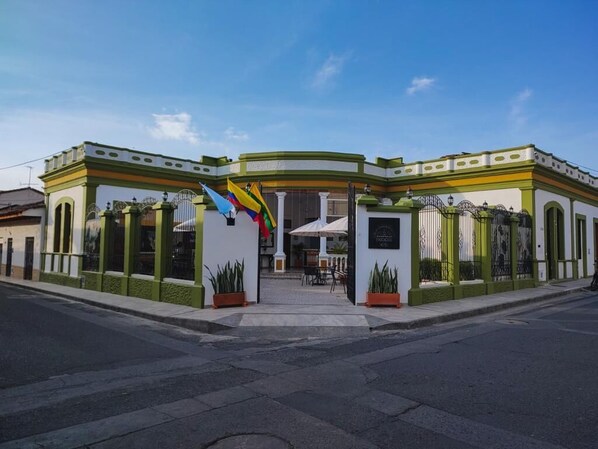 A building with a green and white facade, a central entrance with a colorful sculpture, and a clear sky. - HOTEL EVOCACIÓN (Guadalajara de Buga)
