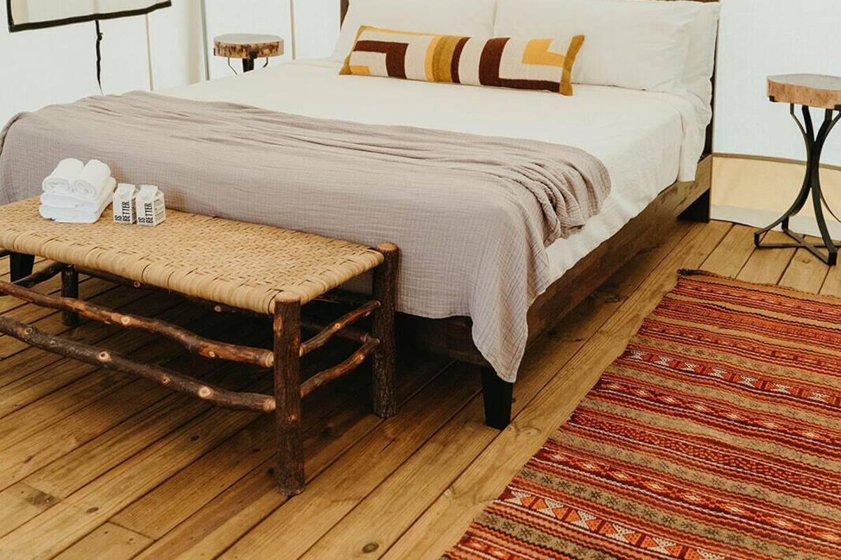A tented room with a bed, a bench, a small table, and a patterned rug.
