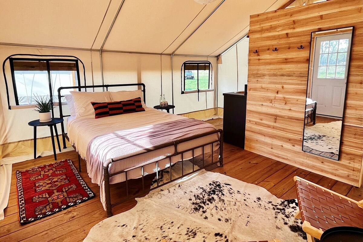 A tent-style bedroom with a bed, bedside tables, a mirror, and a cowhide rug.