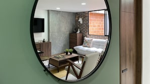 A room with a round mirror, a wooden desk, a chair, a sofa, a TV, and a brick wall. - HOUSINN co-living Fátima (Medellín)