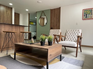 Uma sala de estar moderna com uma mesa de centro de madeira, duas poltronas e uma pequena mesa lateral.
