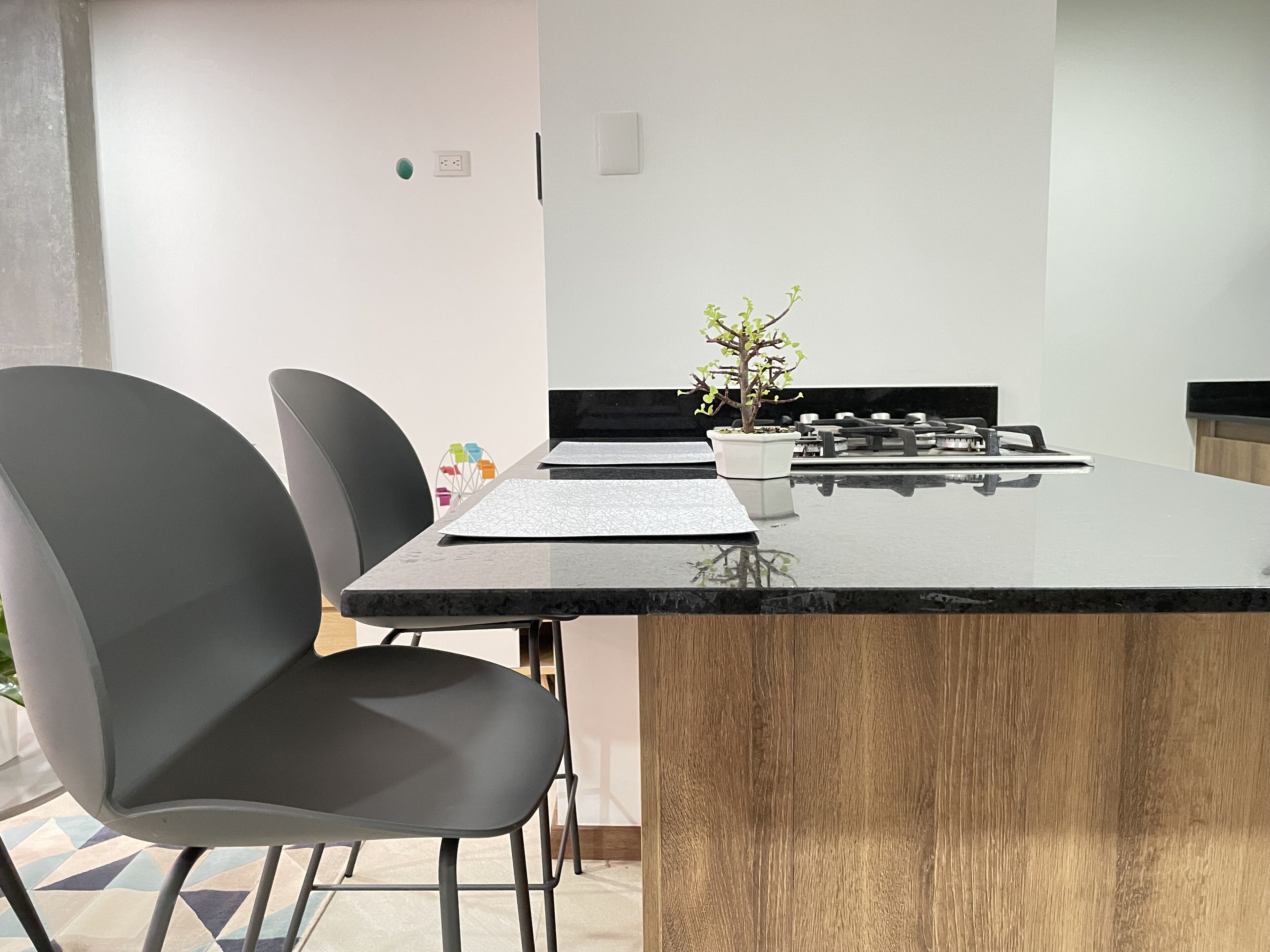 A modern kitchen with a black countertop, a wooden accent, and a small potted plant.