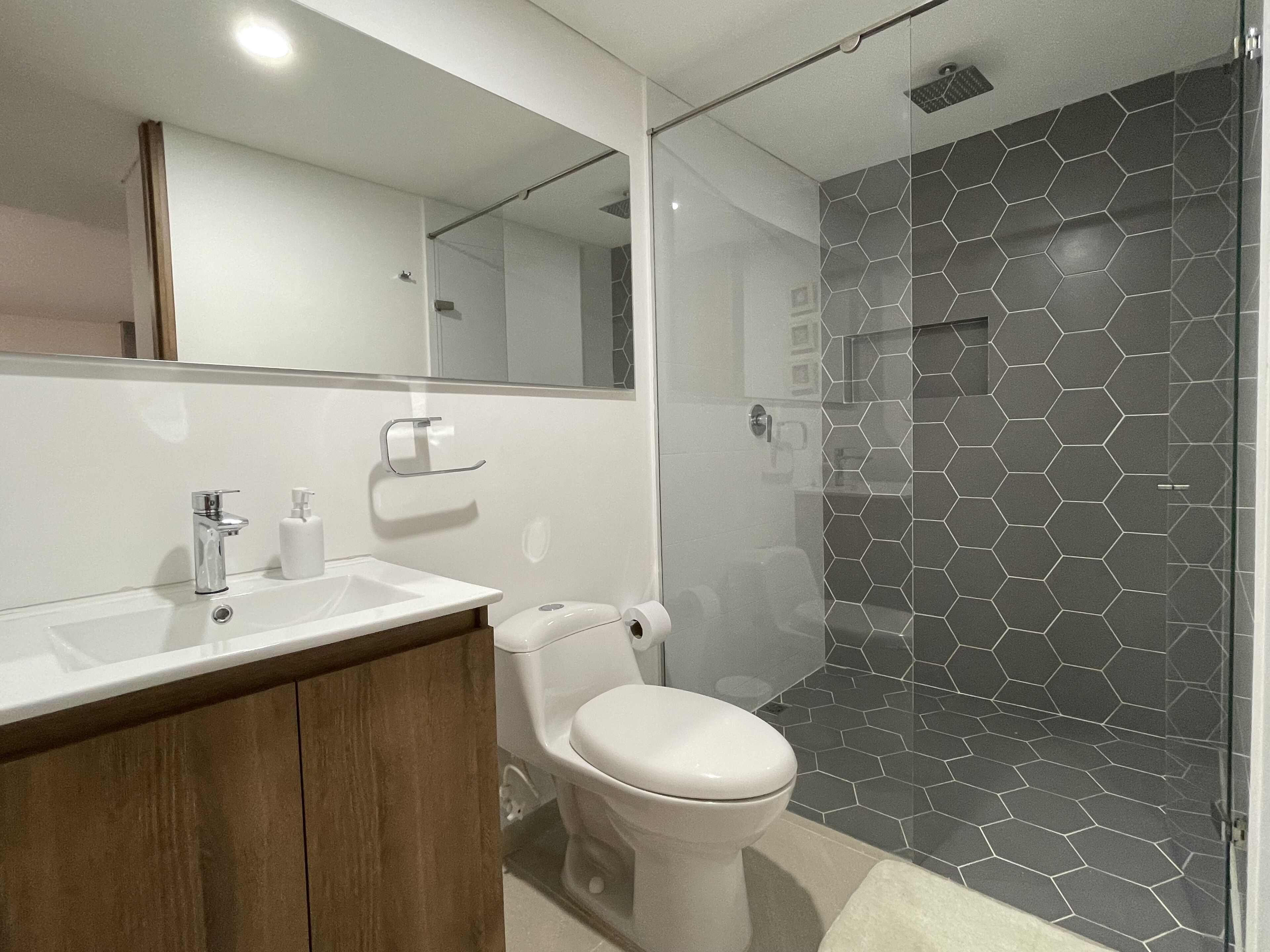 Ein modernes Badezimmer mit einer Duschkabine aus Glas, einer weißen Toilette und einem Holzbadezimmer-Möbel mit Waschbecken.