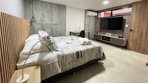 A modern hotel room with a bed, bedside table, lamp, TV, and a small desk with a chair. - HOUSINN co-living Fátima (Medellín)