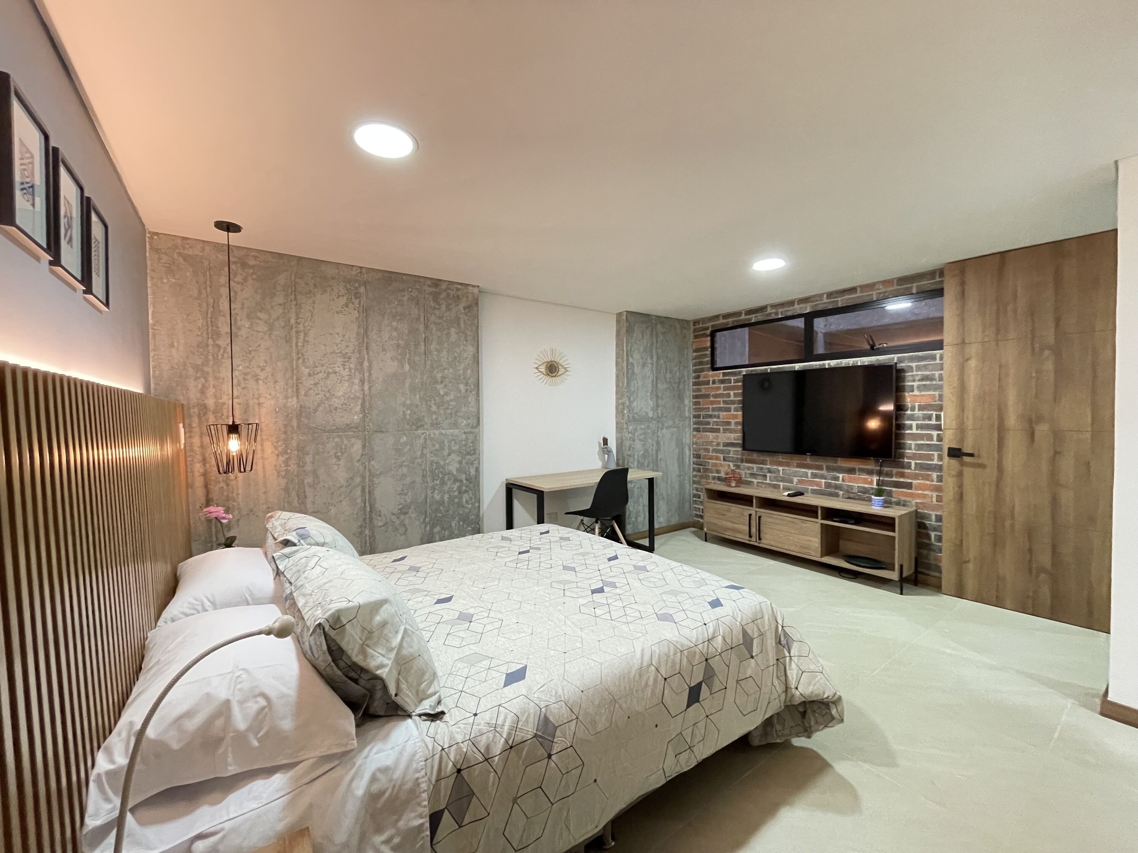 Ein modernes Schlafzimmer mit einem Bett, einem Schreibtisch und einem an einer Ziegelwand befestigten Fernseher.