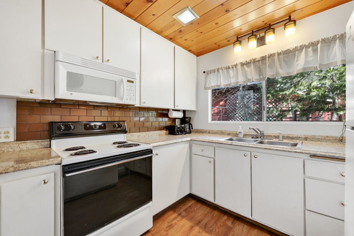 Una cocina con armarios blancos, estufa, microondas y ventana con vista a árboles.
