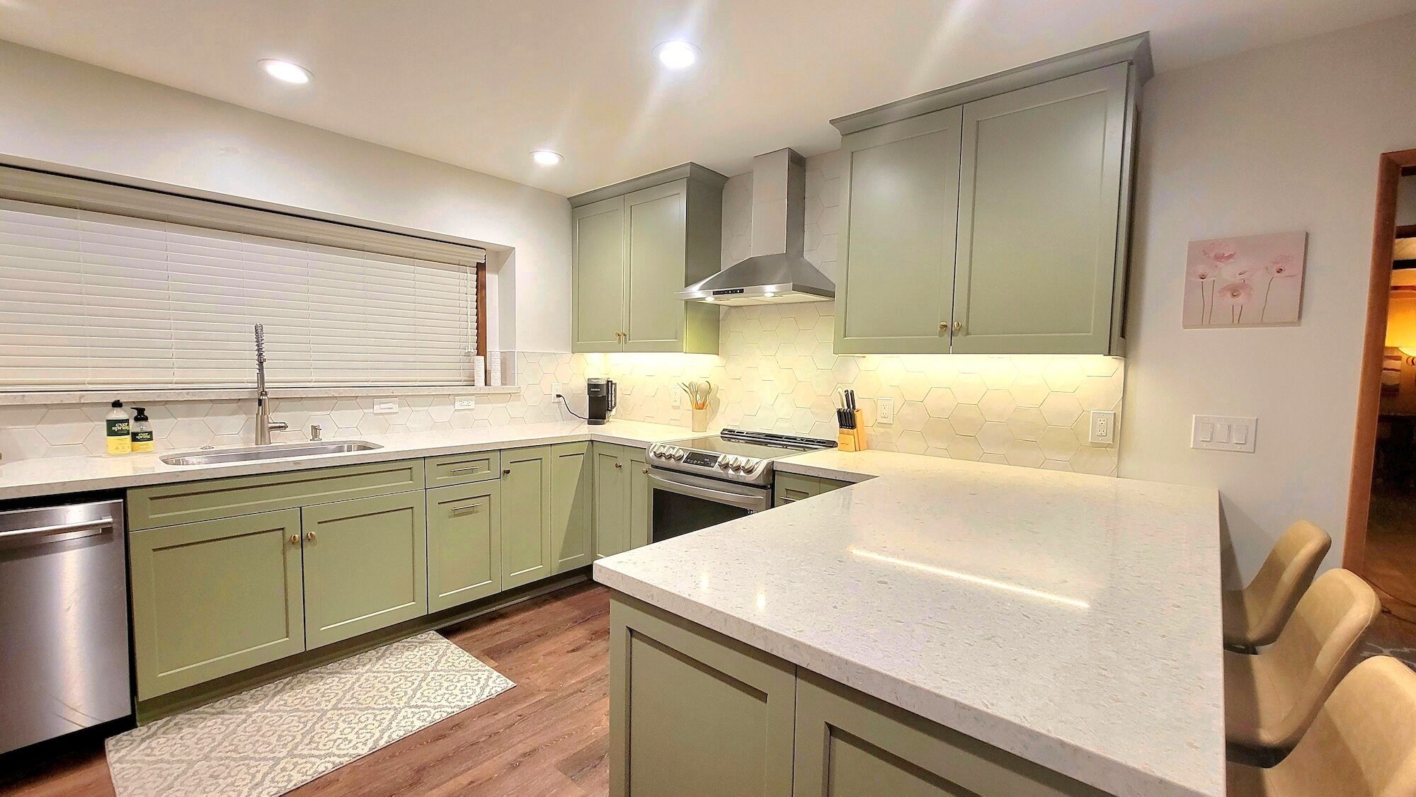 Una cocina moderna con armarios verdes, un lavamanos de acero inoxidable y una encimera amplia.