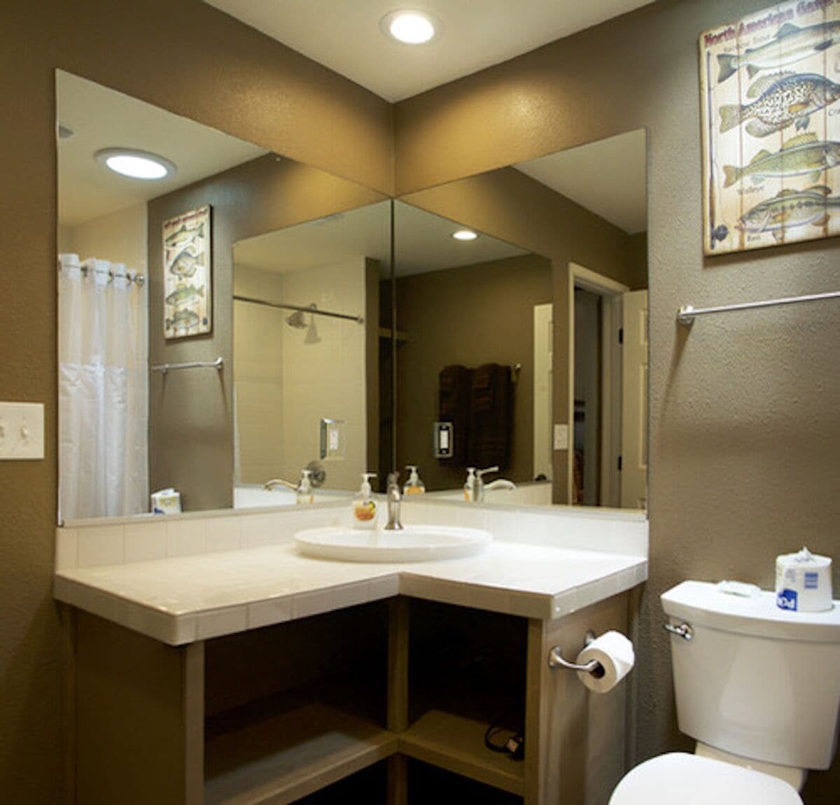 A bathroom with a large mirror, a sink, a toilet, and a shower curtain.