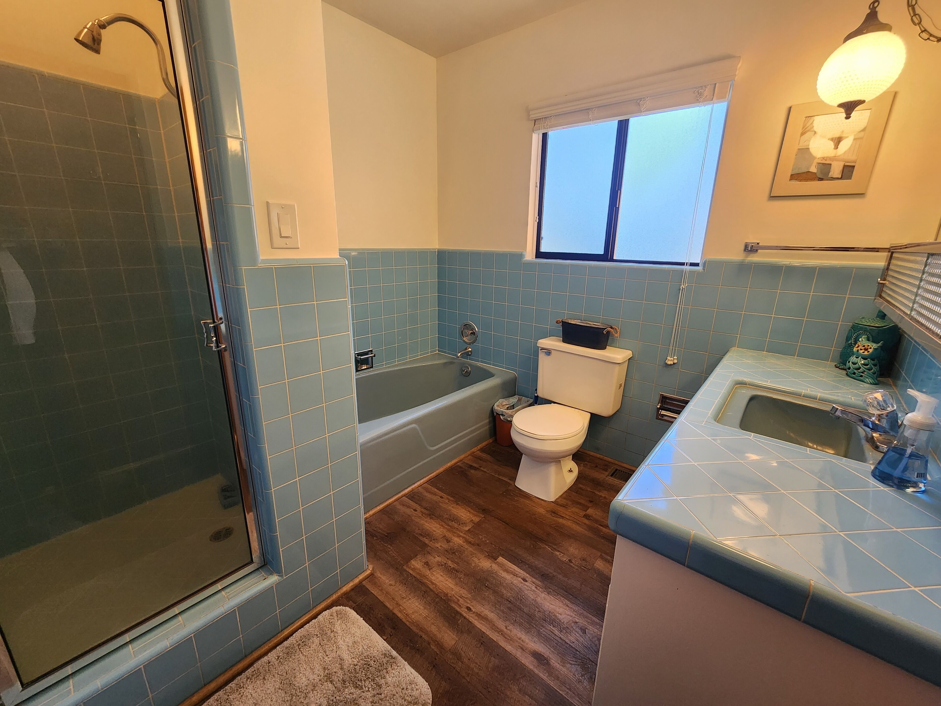 A bathroom with a glass shower enclosure, a bathtub, a toilet, and a sink with a window above the sink.