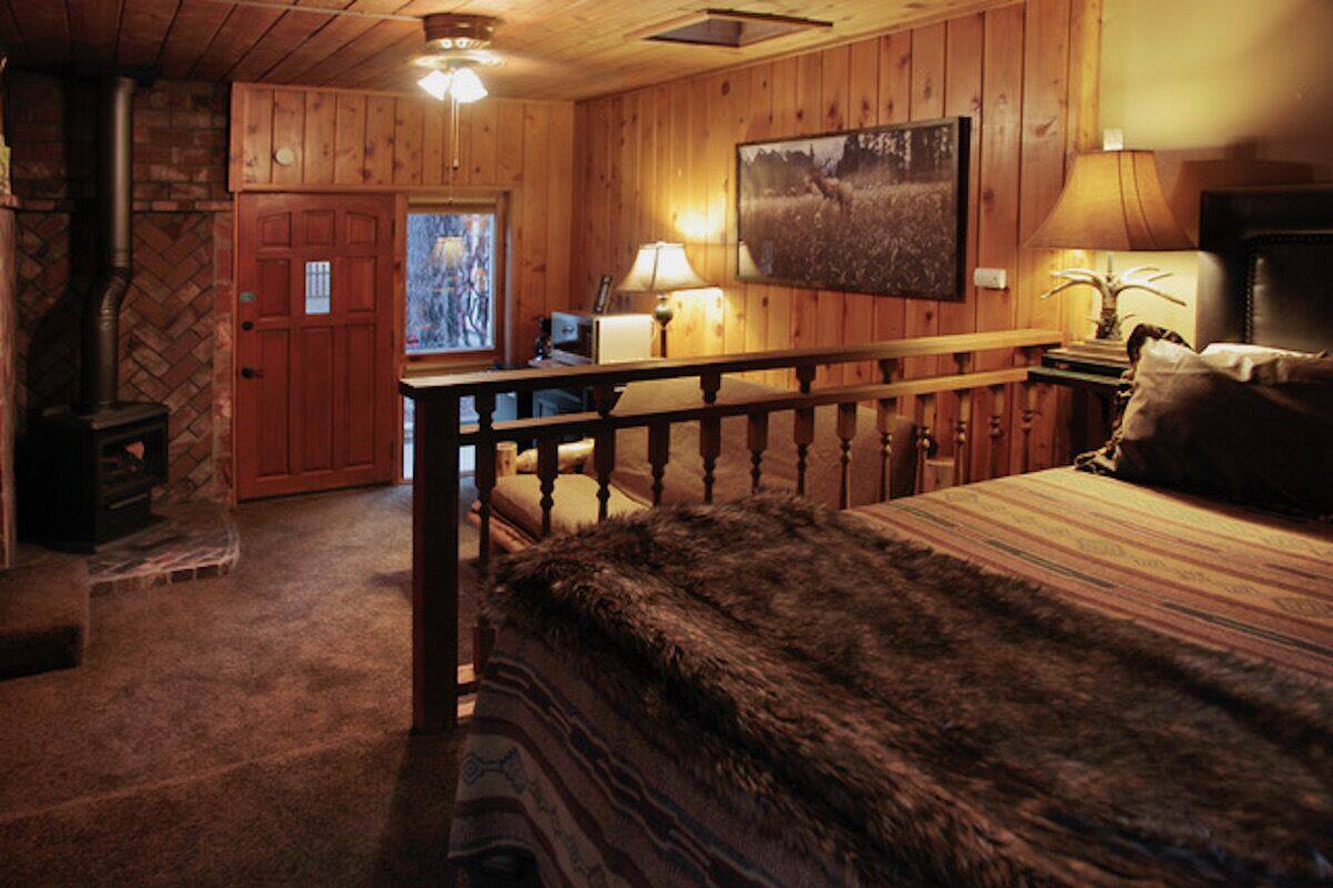A cozy room with a wooden interior, a fireplace, a bed with a fur throw, and a painting on the wall.