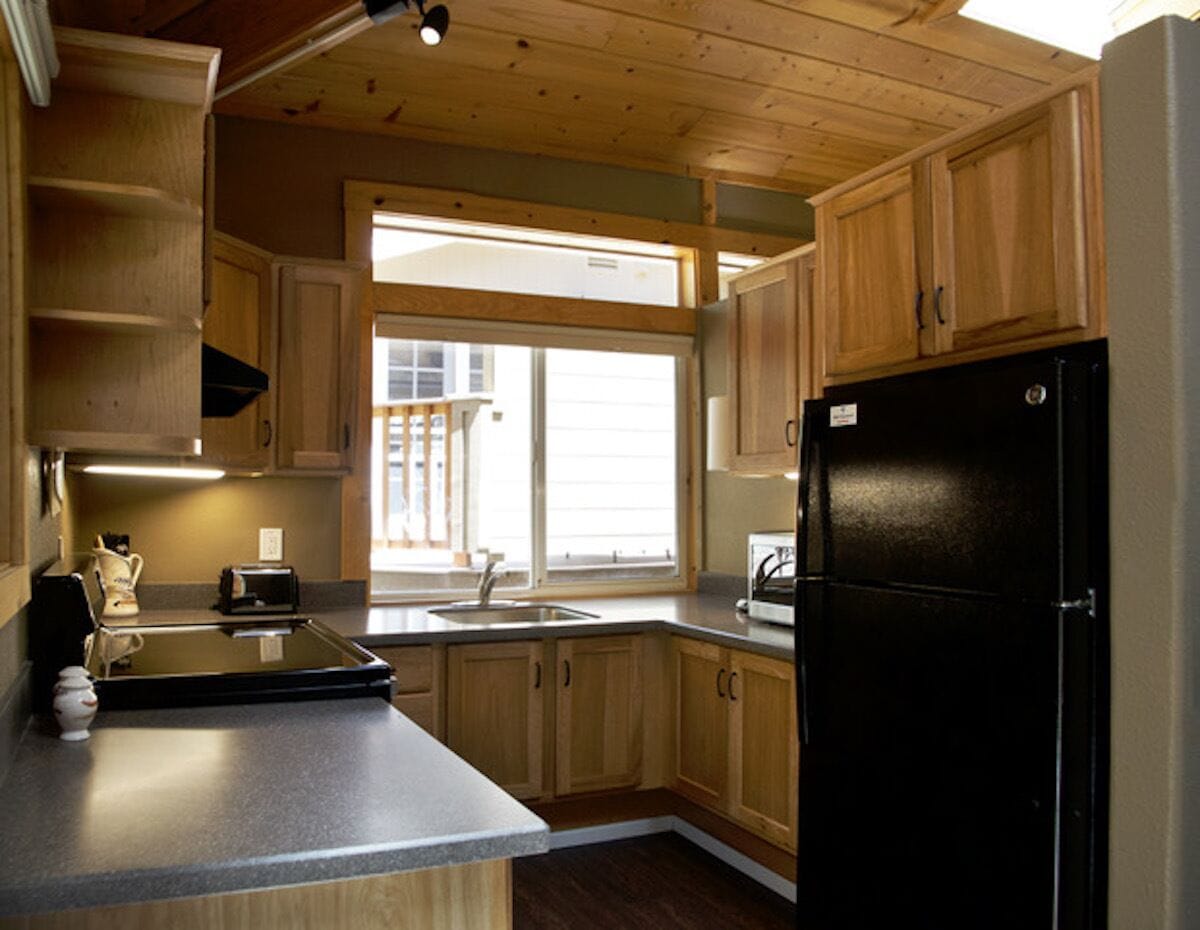 A kitchen with wooden cabinets, a black refrigerator, a window, and a countertop.