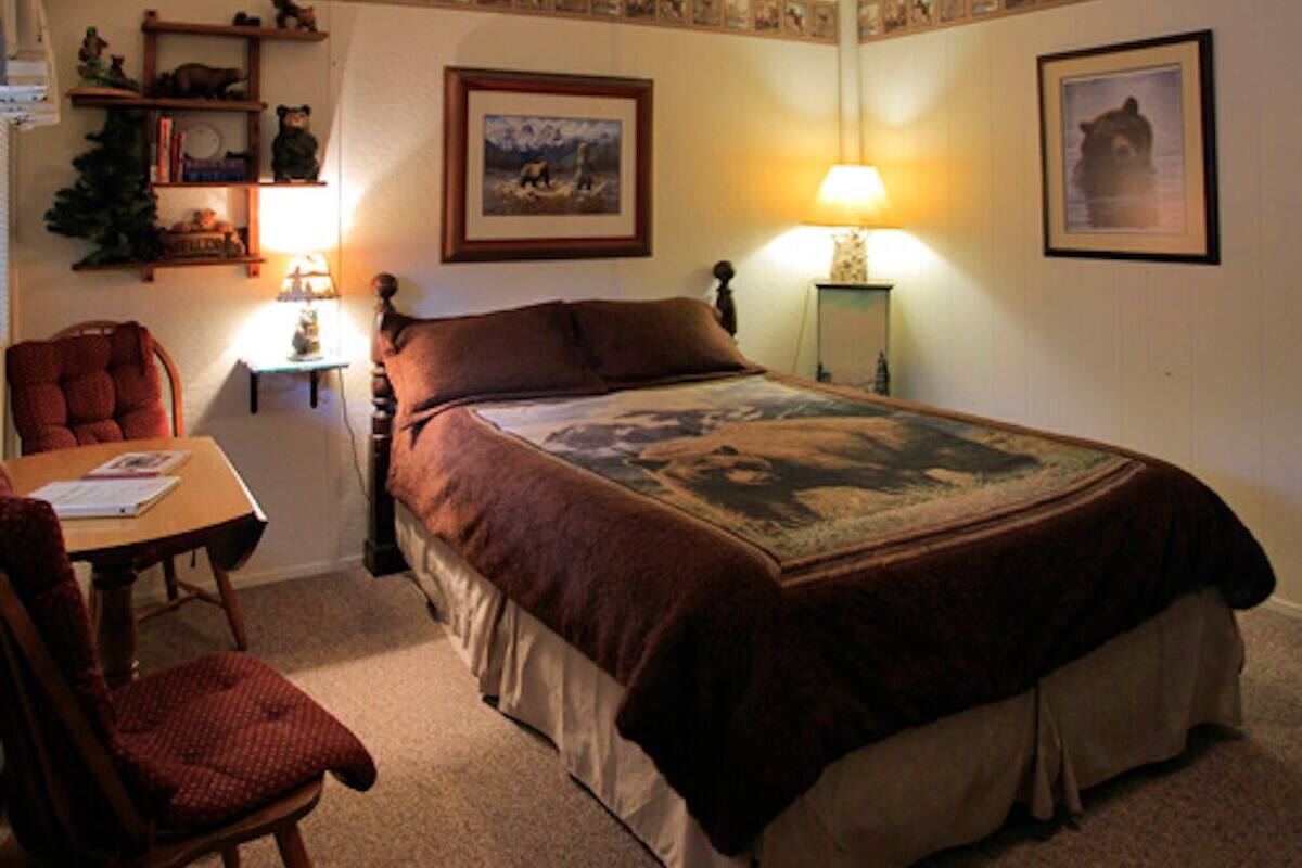 A bedroom with a bed, a desk, a chair, a lamp, and a shelf with decorative items.