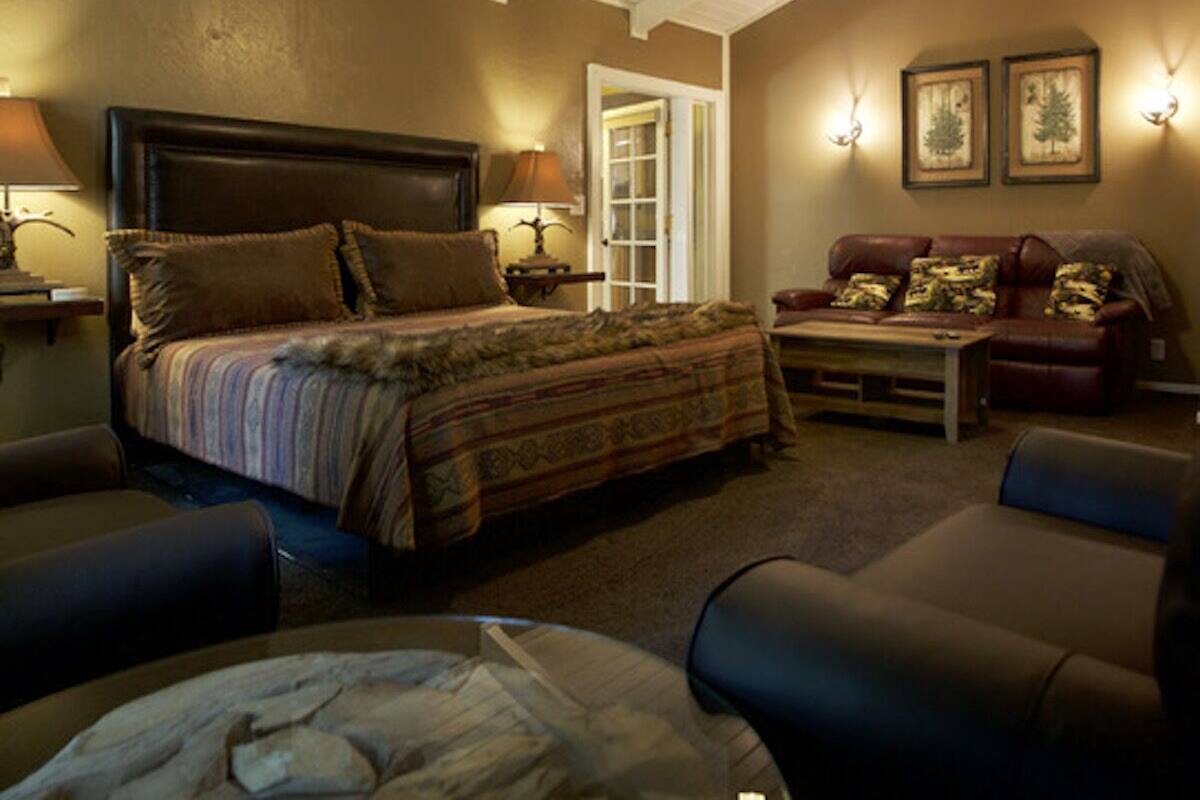 A cozy bedroom with a large bed, a sitting area with a sofa and armchairs, and a ceiling with exposed beams.