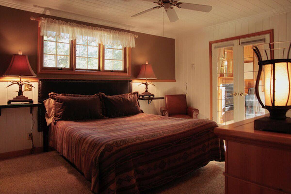 A bedroom with a large bed, two bedside lamps, a ceiling fan, and a window with a lace curtain.
