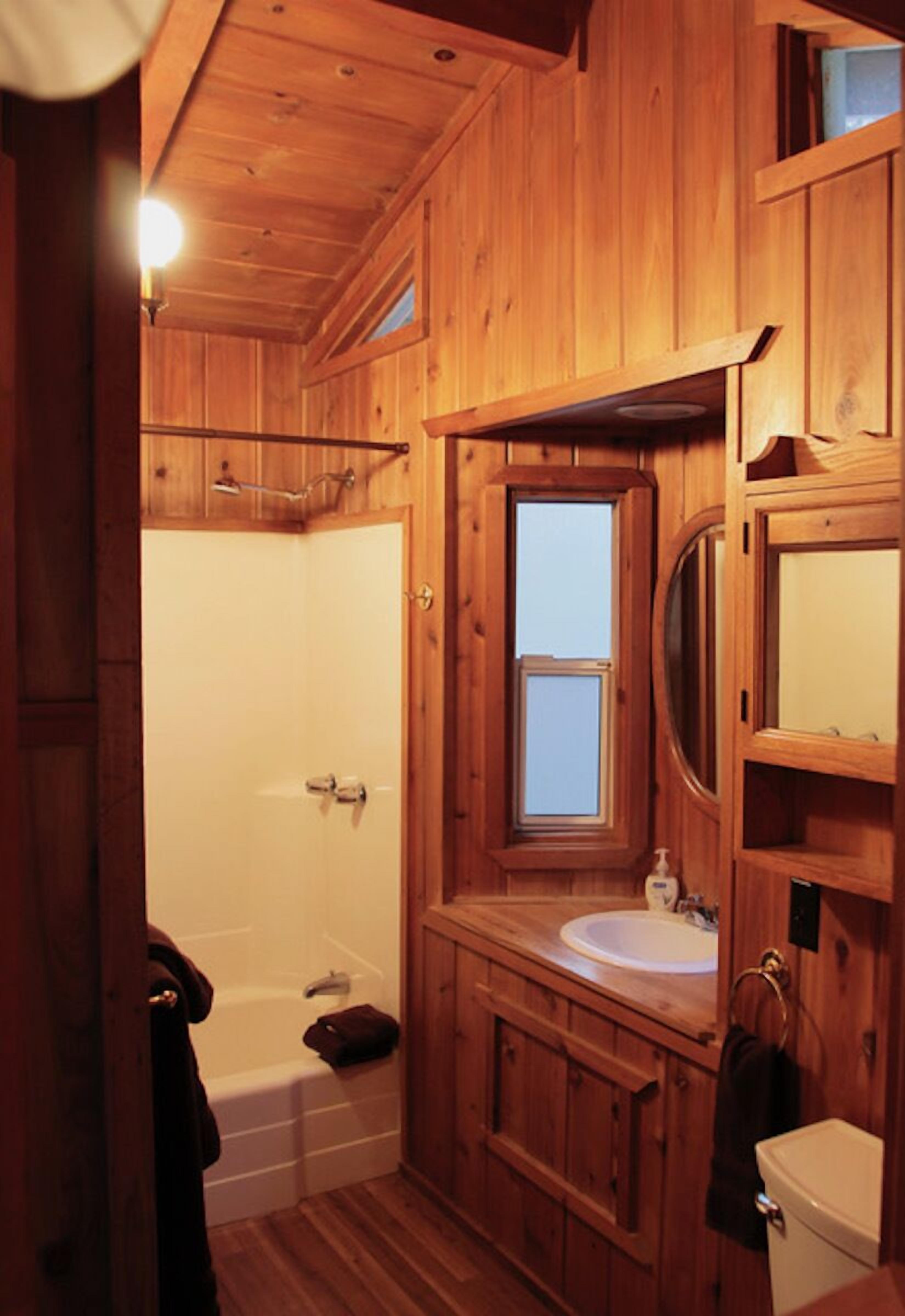 Une salle de bain rustique, aménagée dans une cabane en bois, avec une baignoire, un lavabo et des toilettes.