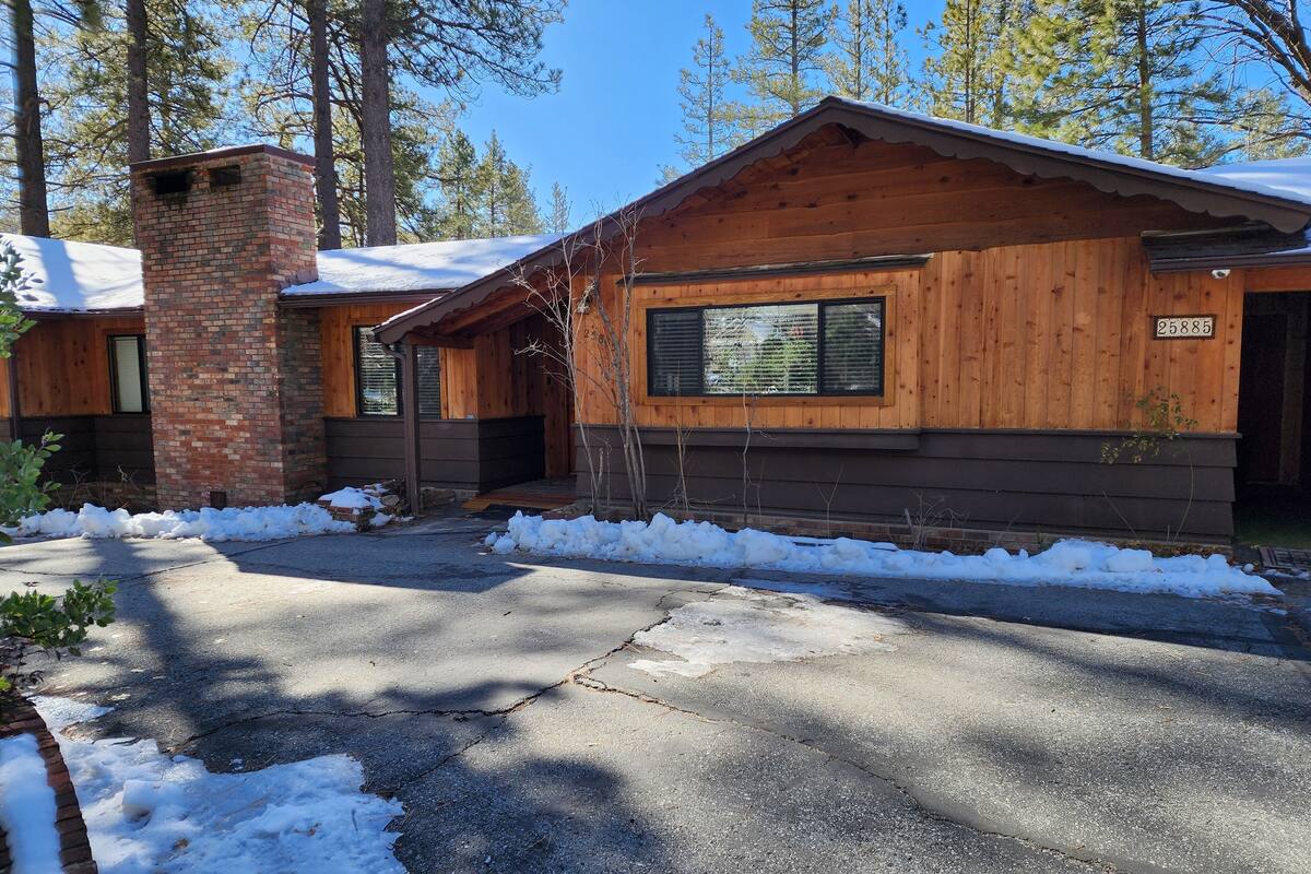 A wooden cabin with a brick chimney, a garage, and a snow-covered driveway.