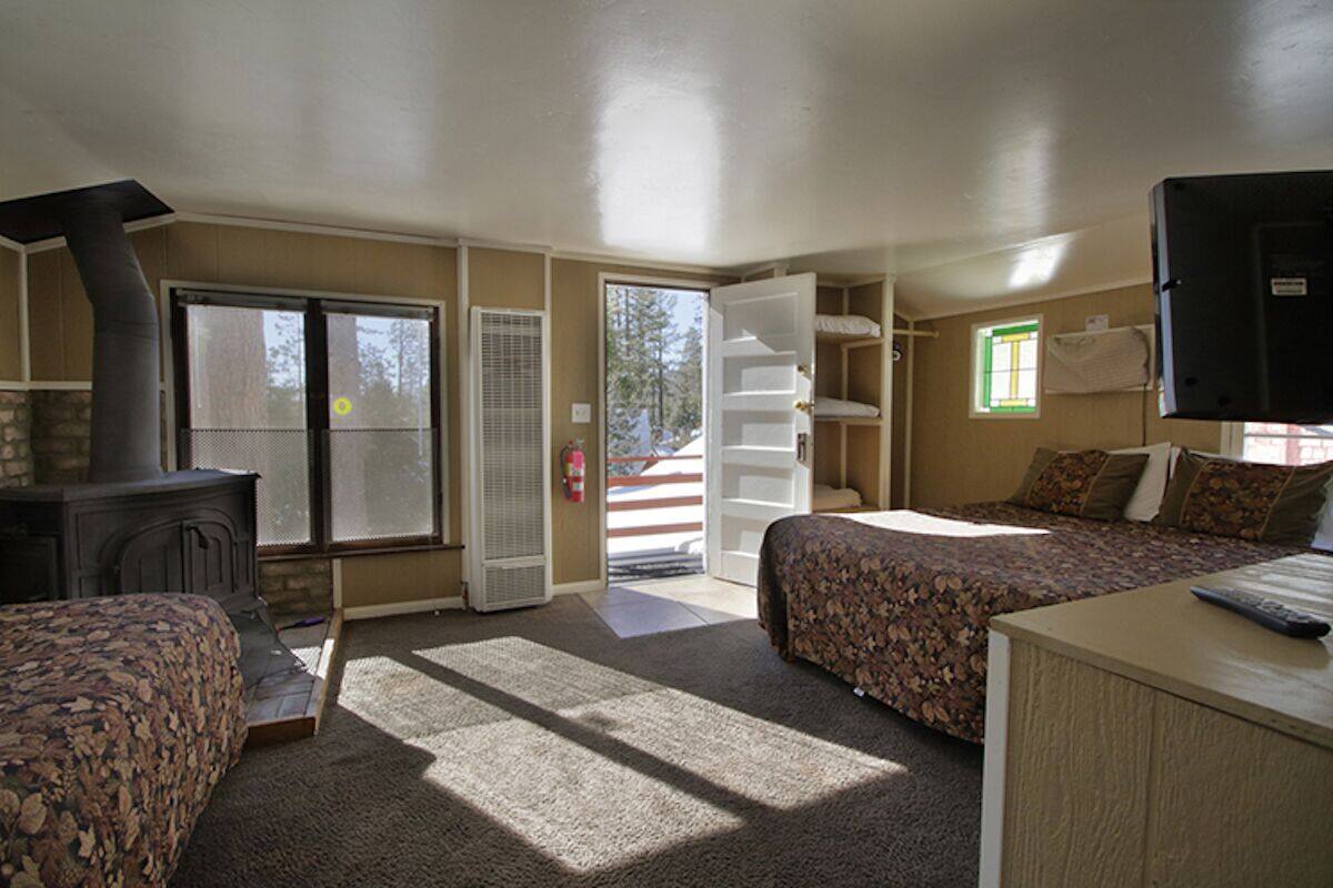 A room with two beds, a fireplace, a television, and a large window.