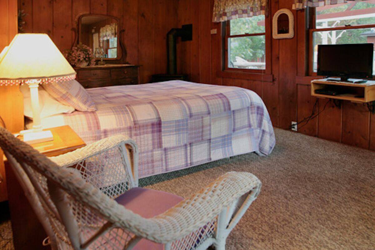 A cozy bedroom with a bed, a chair, a lamp, a television, and a window with curtains.