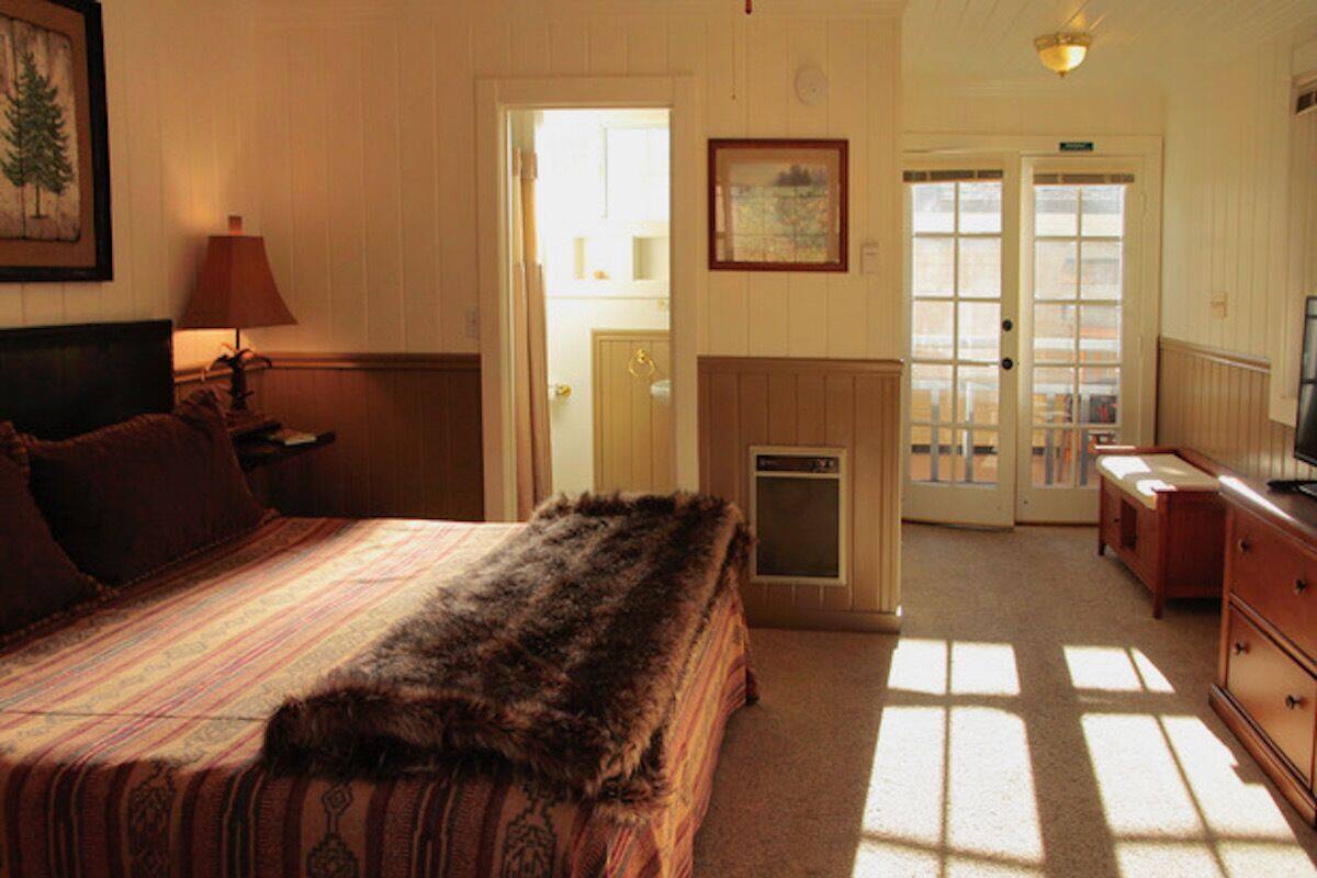 A bedroom with a large bed, a fireplace, a television, and a door leading to a balcony.