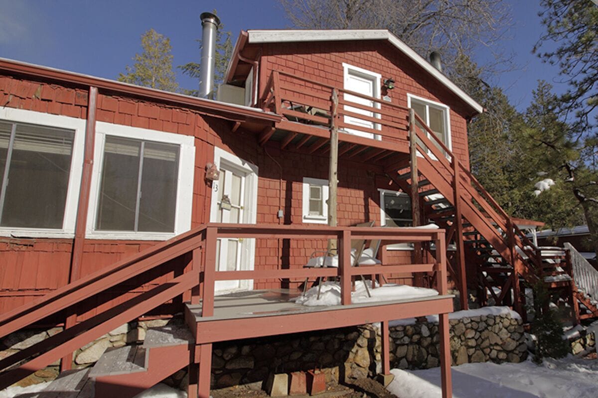 Eine rote Holzhütte mit steinernem Fundament, einem Balkon und einer Holztreppe.