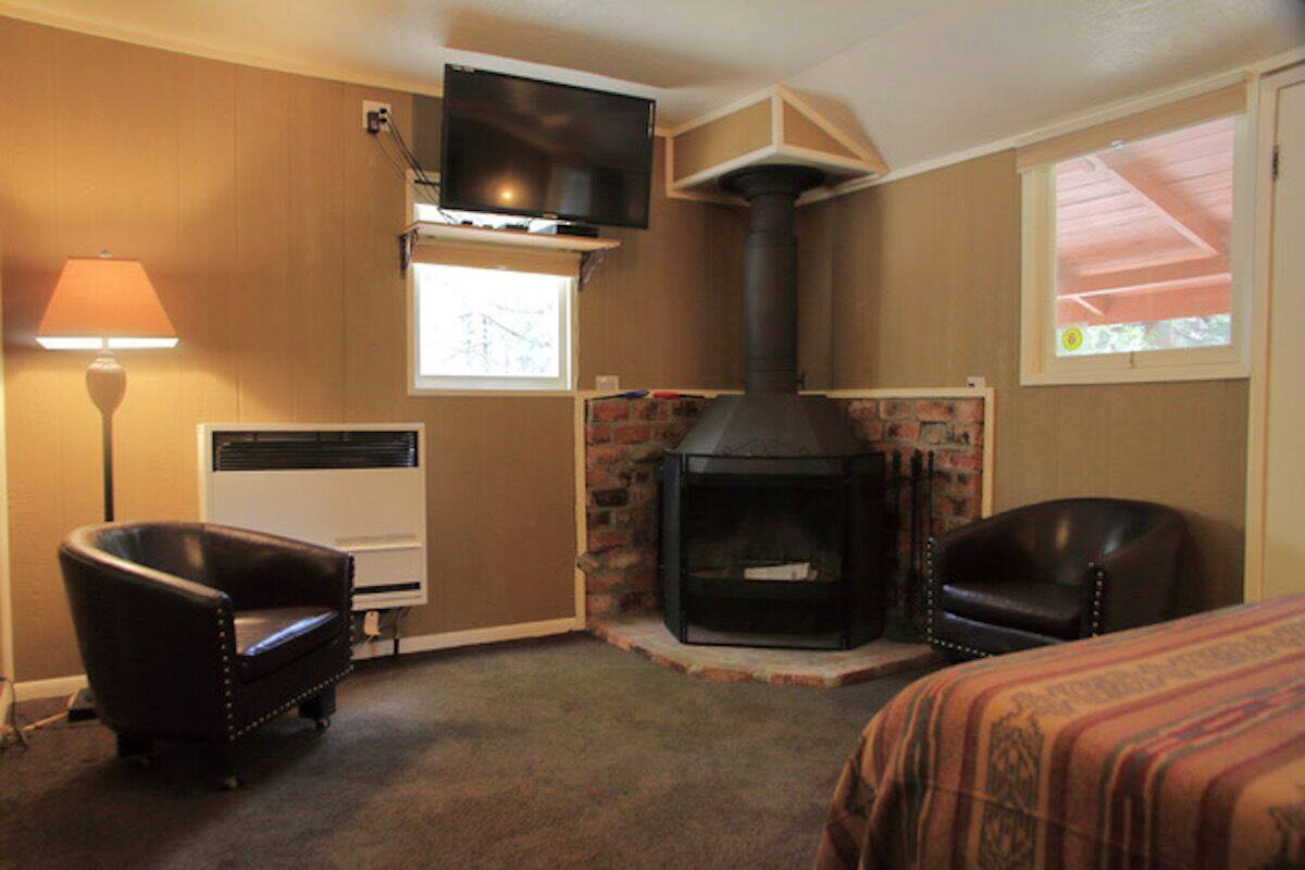 A room with a fireplace, two leather chairs, a TV mounted on the wall, and a window with a view.