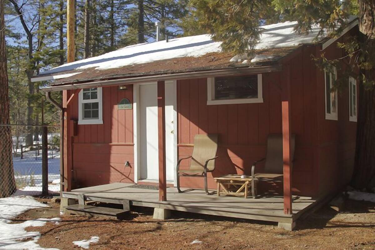 A small, single-story cabin with a porch, a door, and two chairs.