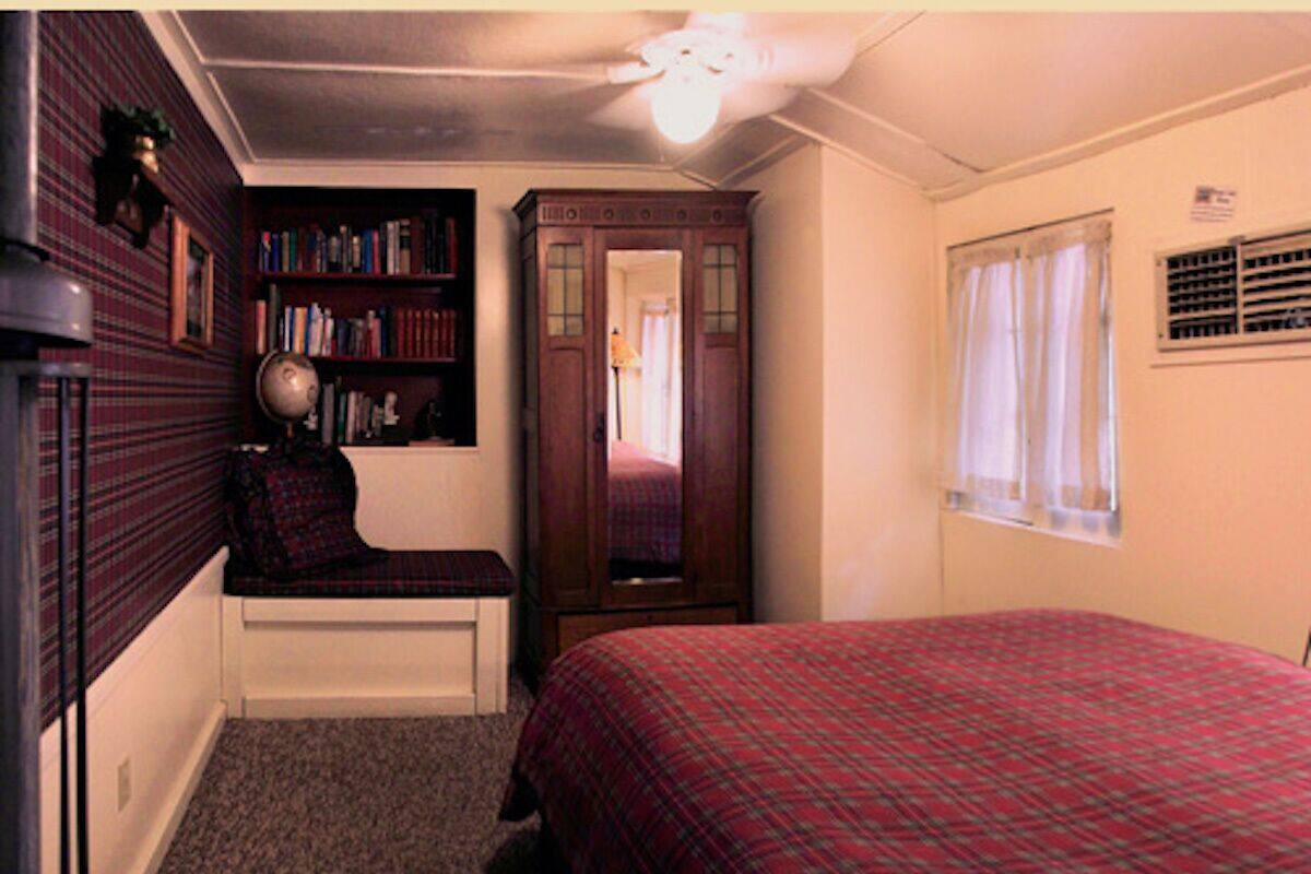 A bedroom with a bed, a bookshelf, a desk, a mirror, and a window.
