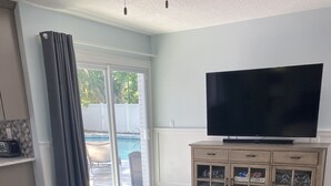 A living room with a leather sofa, a round coffee table, a TV on a wooden cabinet, and a sliding glass door leading to a pool. - Pool Home near Ponte Vedra Beach! (Ponte Vedra Beach)