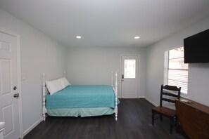 A bedroom with a bed, a chair, a desk, and a TV mounted on the wall.