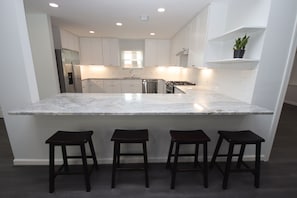 A modern kitchen with white cabinets, a marble island, and three stools.