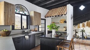 A modern kitchen with dark cabinetry, a large island, and a rustic ceiling.