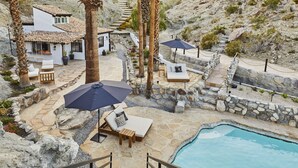 A poolside area with lounge chairs, umbrellas, and a stone pathway leading to a house.