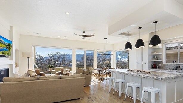A modern kitchen with a large island, white bar stools, and a dining area with a view of mountains.