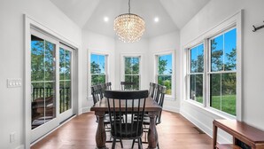 A spacious dining area with a large wooden table and chairs, large windows offering views of greenery, and a chandelier hanging from the ceiling. - Cliffside Cottage, Private Pond, 50 acres w/ Breathtaking views near Galena, IL (Elizabeth)