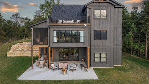 A modern two-story house with a stone staircase leading to the entrance, a covered patio with outdoor furniture, and a large window overlooking the yard. - Cliffside Cottage, Private Pond, 50 acres w/ Breathtaking views near Galena, IL (Elizabeth)