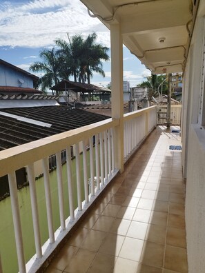 Un balcon doté d’un sol carrelé, d’une balustrade blanche et offrant une vue sur un toit végétalisé avec des palmiers.