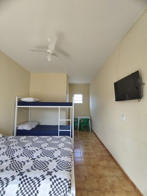 A dormitory room with bunk beds, a ceiling fan, a television, and a small table with chairs. - Suítes Córdoba (Bertioga)