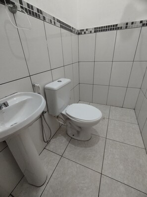 A bathroom with a white sink, toilet, and tiled walls. - Suítes Córdoba (Bertioga)