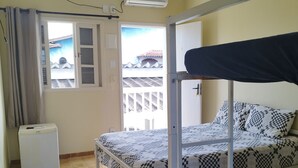 Una habitación con una cama litera, un pequeño aire acondicionado blanco, una ventana con cortinas y un ventilador de techo.